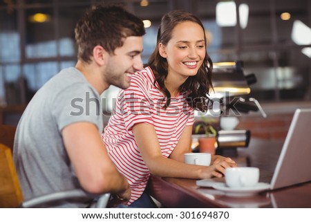 Smiling friends using laptop and having coffee together at coffee shop