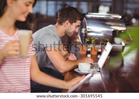 Smiling young man sitting at bar and using laptop in a cafe