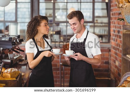 Smiling waiter and waitress holding cup of coffee at coffee shop