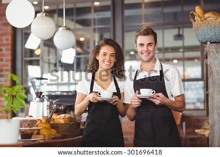 Portrait of smiling waiter and waitress holding cup of coffee at coffee shop