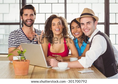 Portrait of smiling friends standing around laptop at coffee shop