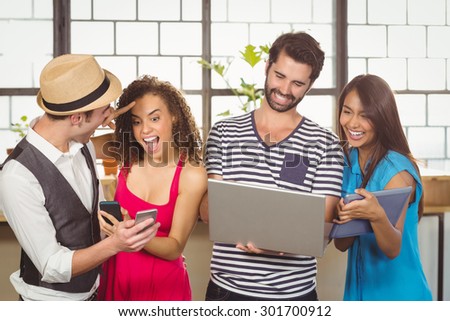 Laughing friends using different types of multimedia at coffee shop