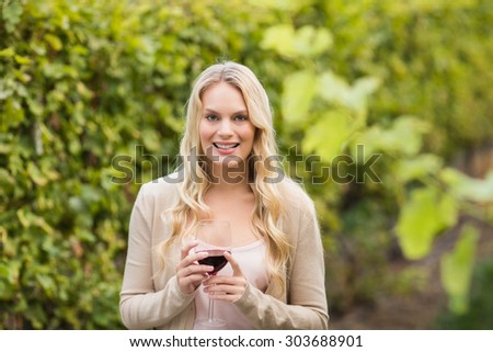 Young happy woman holding a glass of wine and looking at camera in the grape fields