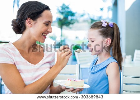 Mother feeding her daughter with cake at the cafe
