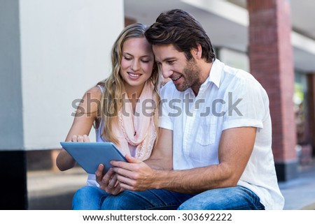 Smiling couple sitting and using tablet computer together at shopping mall