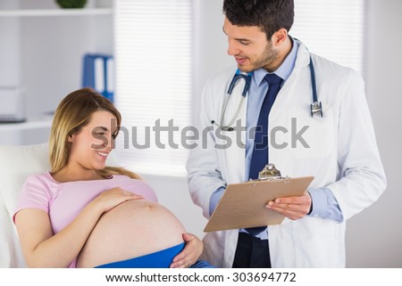 Smiling doctor giving advice to lying pregnant patient in medical office