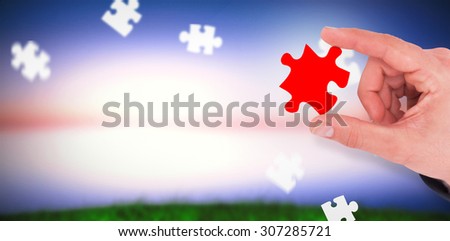 Businessman measuring something with his fingers against green grass under blue and purple sky