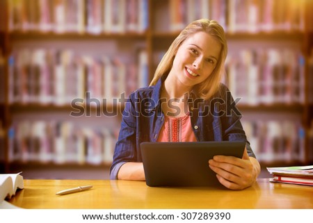 Student studying in the library with tablet against books on desk in library