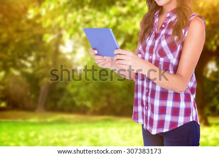 Happy pretty brunette using tablet computer against trees and meadow in the park