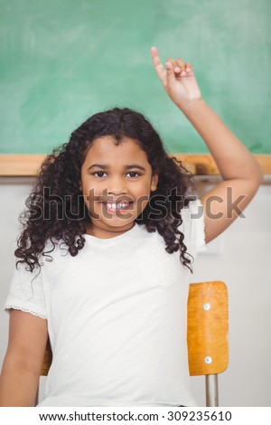 Portrait of cute pupil raising hand in a classroom in school