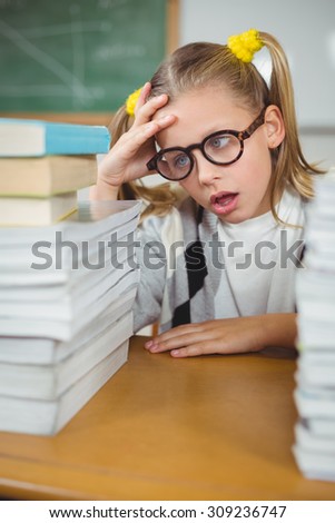 Overwhelmed pupil between stack of books on her desk in a classroom