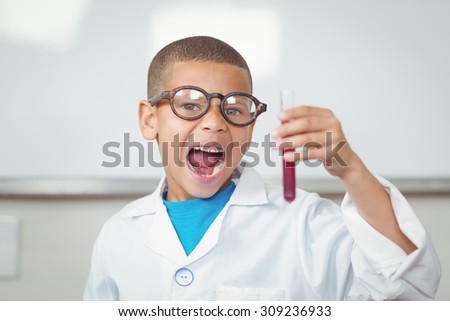 Portrait of surprised pupil with lab coat looking at test tube in a classroom