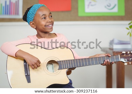 Smiling pupil playing guitar in a classroom in school
