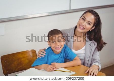 Portrait of smiling teacher and her pupil sitting at desk in a classroom