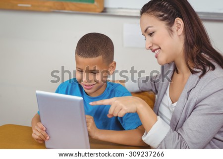 Pretty teacher and pupil using tablet at his desk in a classroom