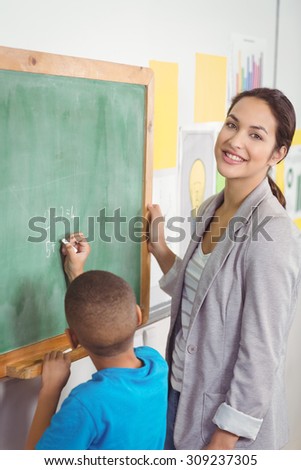 Portrait of pretty teacher helping pupil at chalkboard in a classroom