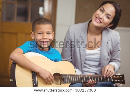 Portrait of pretty teacher giving guitar lessons to pupil in a classroom