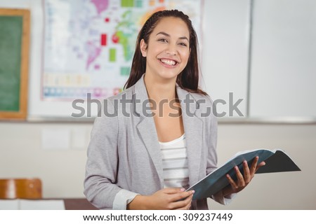 Portrait of pretty teacher holding notebook in a classroom in school