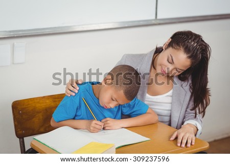Pretty teacher helping pupil at his desk in a classroom