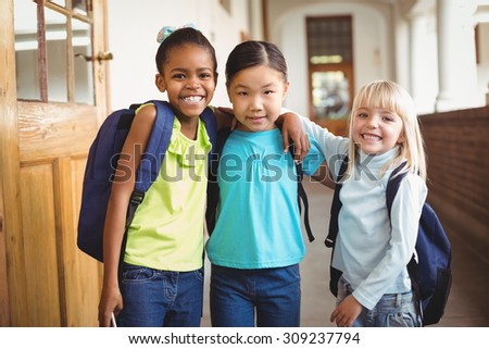 Portrait of cute pupils with arms around at corridor in school