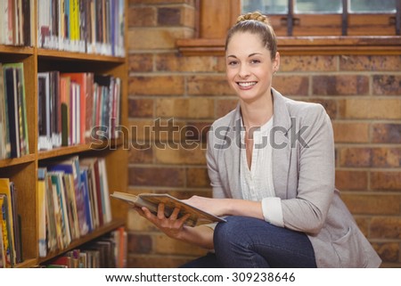 Portrait of blonde teacher searching book in the library in school
