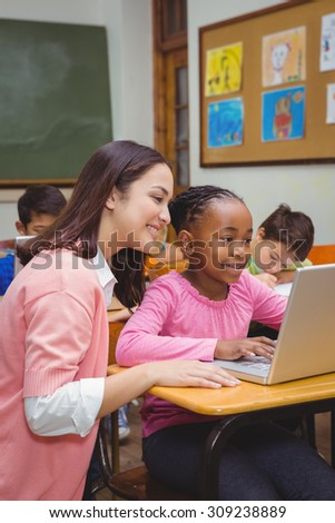 Happy teacher using laptop with student at the elementary school