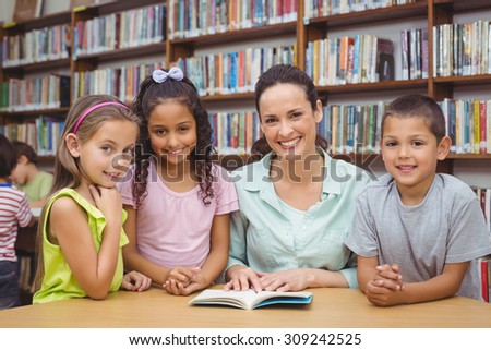 Pupils and teacher reading book in library at the elementary school