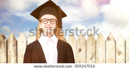 Cute pupil in graduation robe against fence under blue sky