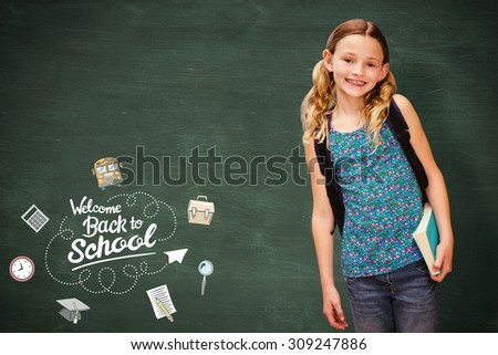 Cute little girl holding book in library against green chalkboard