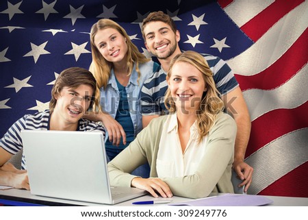 Students using laptop in classroom against digitally generated american national flag