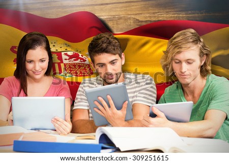 College students using digital tablets in library against digitally generated spain flag rippling