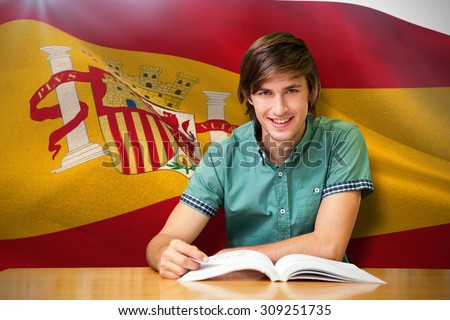 Student sitting in library reading against digitally generated spanish national flag