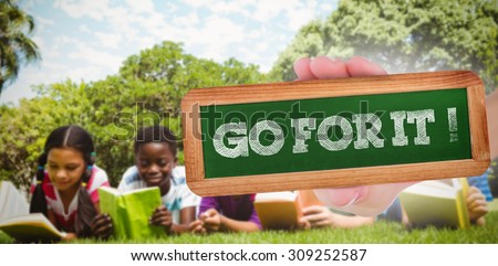 The word go for it! and hand showing chalkboard against children lying on grass and reading books