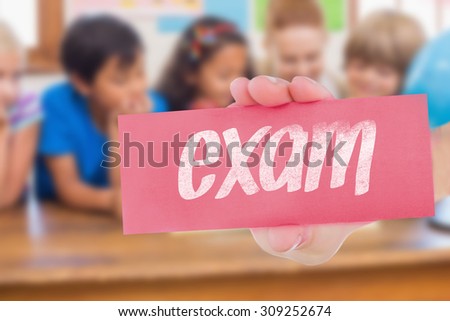 The word exam and hand showing card against cute pupils and teacher smiling at camera in classroom