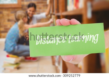 The word distance learning and hand showing card against teacher and little girl selecting book in library
