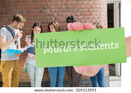 The word mature students and hand showing card against happy students standing and reading