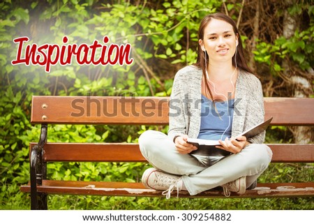 The word inspiration against smiling student sitting on bench listening music with mobile phone and holding book