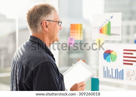 Smiling businessman looking flow charts on the wall at office