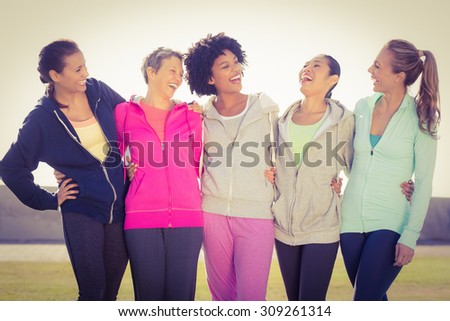 Laughing sporty women with arms around each other in parkland