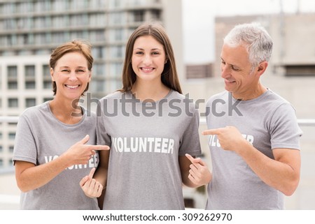Portrait of smiling volunteers pointing on shirt on roof of building