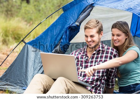 Young pretty hiker couple sitting in a tent looking at laptop in the nature