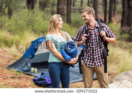 Young pretty hiker couple holding a sleeping bag and backpack in the nature