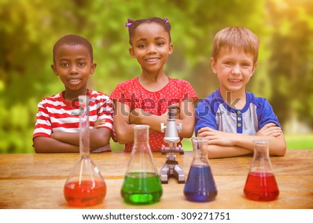 Cute pupils standing with arms crossed behind beaker against trees and meadow