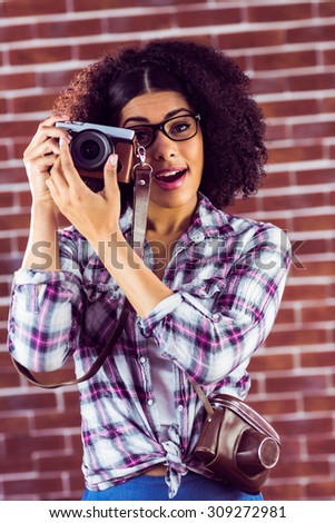 Portrait of attractive hipster photographing with camera against red brick background
