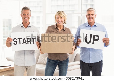 Portrait of smiling casual business people holding start up sign in the office