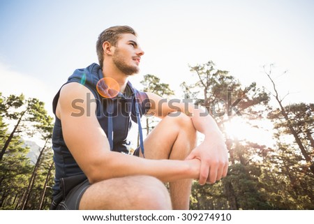 Young happy jogger sitting on rock and looking away in the nature