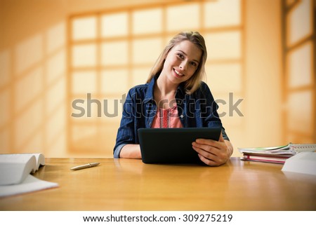 Student studying in the library with tablet against room with large windows showing city