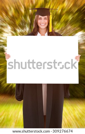 Full length of a woman holding a blank sheet in front of her as she smiles against trees and meadow in the park