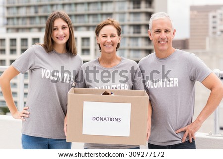 Portrait of smiling volunteers holding donation box on roof of building