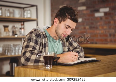 Hipster having coffee and writing in planner at coffee shop